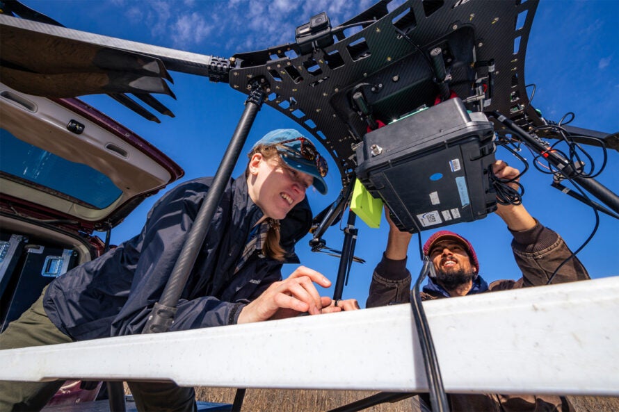 Emily Follansbee and James Lee from Los Alamos National Laboratory prepare a drone for field surveys. The drone must be programmed using a tiny onboard computer and screen.